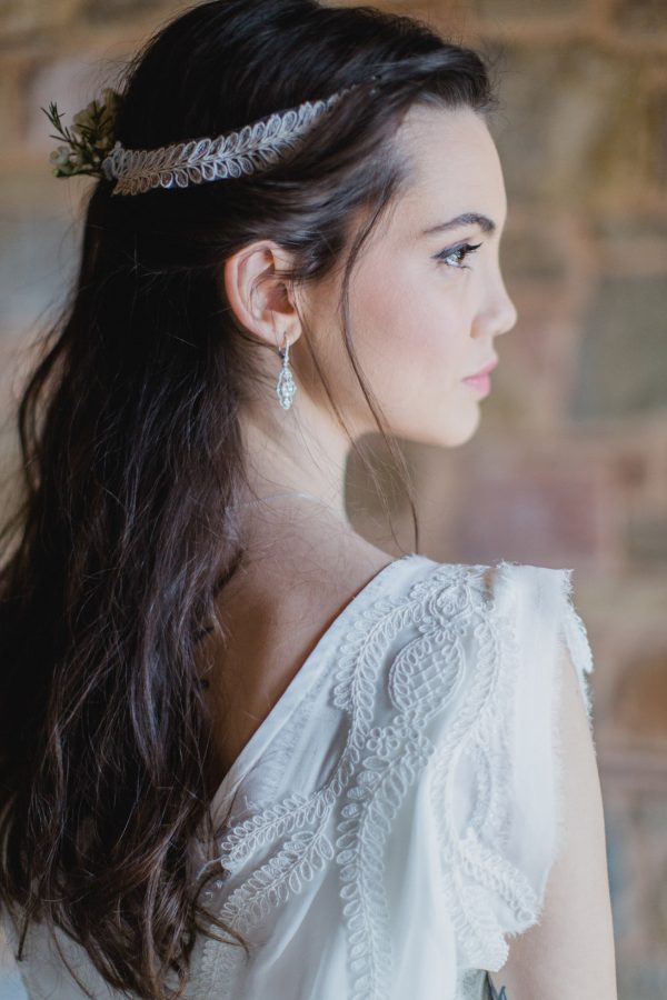 Bride in her wedding dress, hair and make-up and jewellery posing for elegant portraits facing the window.