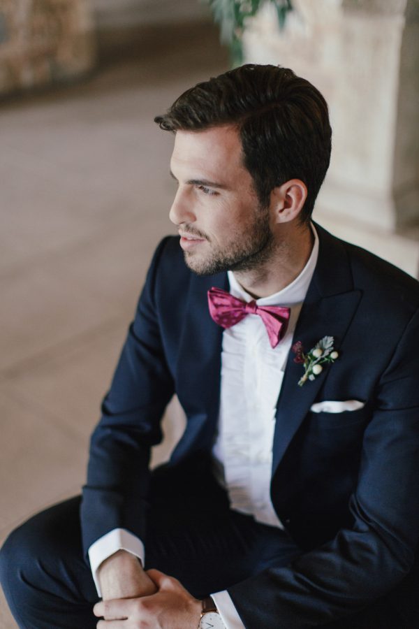 Groom in his wedding suit by Uomo Sartoriale Athens posing for elegant portraits sitting in an armchair facing the window.