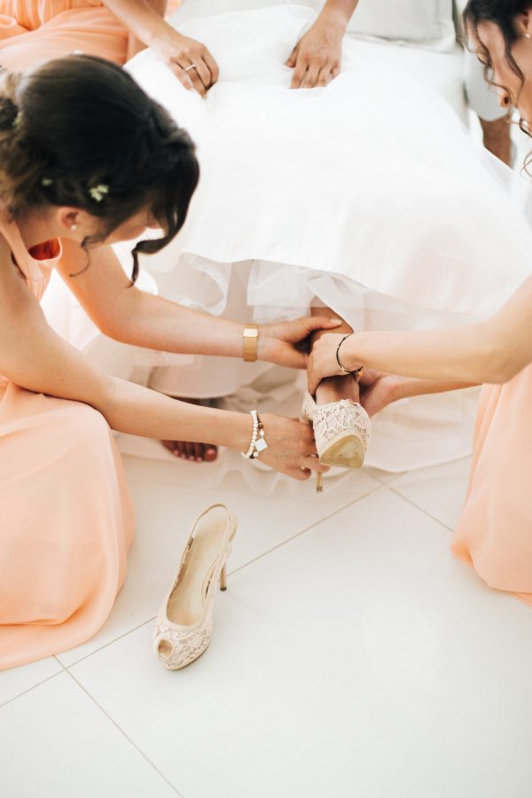 Professional wedding day of bridesmaids dressing up the bride and putting on her high heeled shoes.