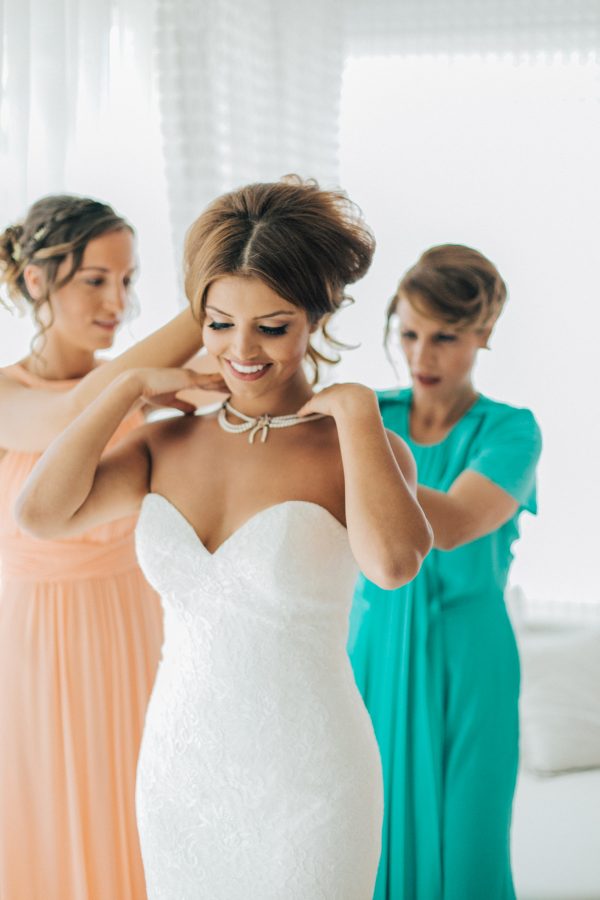 Professional wedding day portrait, beautiful smiling bride being dressed up by her mother and one of the bridesmaids.