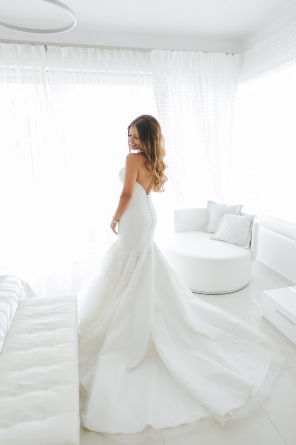 Professional wedding day portrait, beautiful smiling bride posing for the wedding photographer in her luxury bridal villa suite in Crete against white windows.