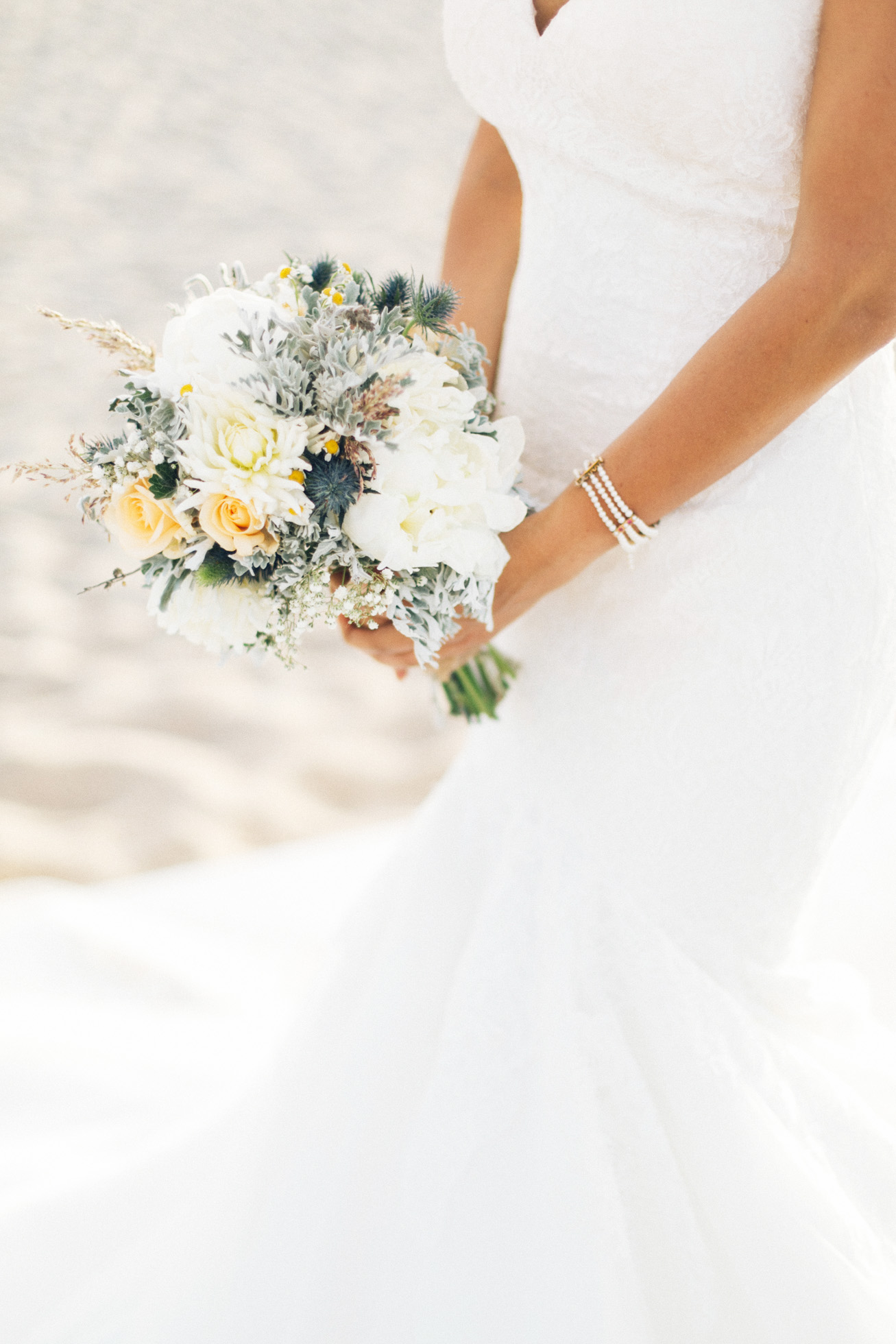 Professional Crete wedding photoshoot, closeup image of the bride holding her bouquet on the beach and posing for photographer.