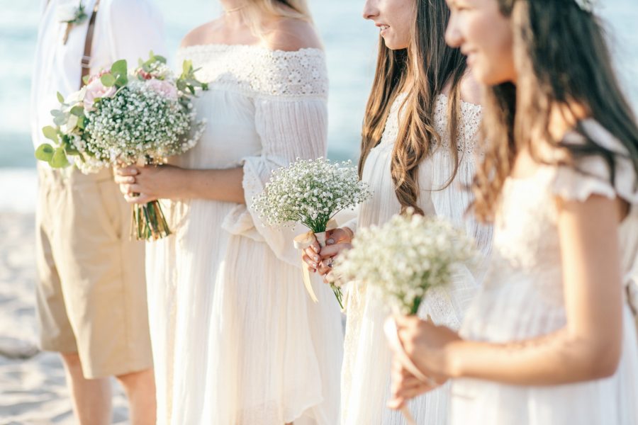 Close up photo of bridesmaids standing on the beach and holding their delicate understated bouquets of seasonal flowers.