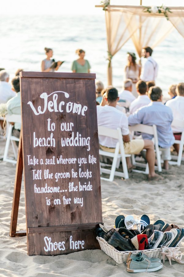 Welcome to our beach wedding sign with the bride and groom and teir guests in the background during a symbolic ceremony in Rethymno Crete.