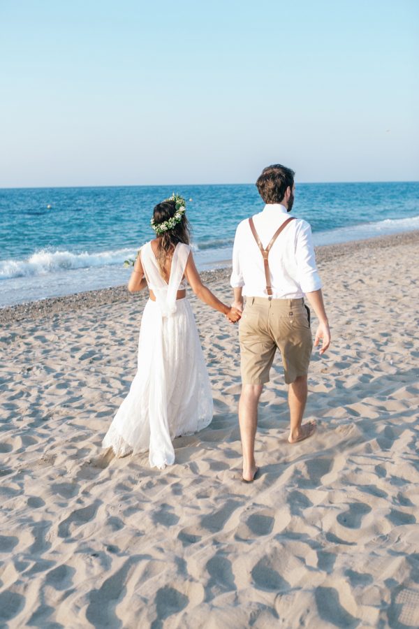 Professional image of bride and groom walking along a sandy beach in Crete after their beach wedding ceremony.