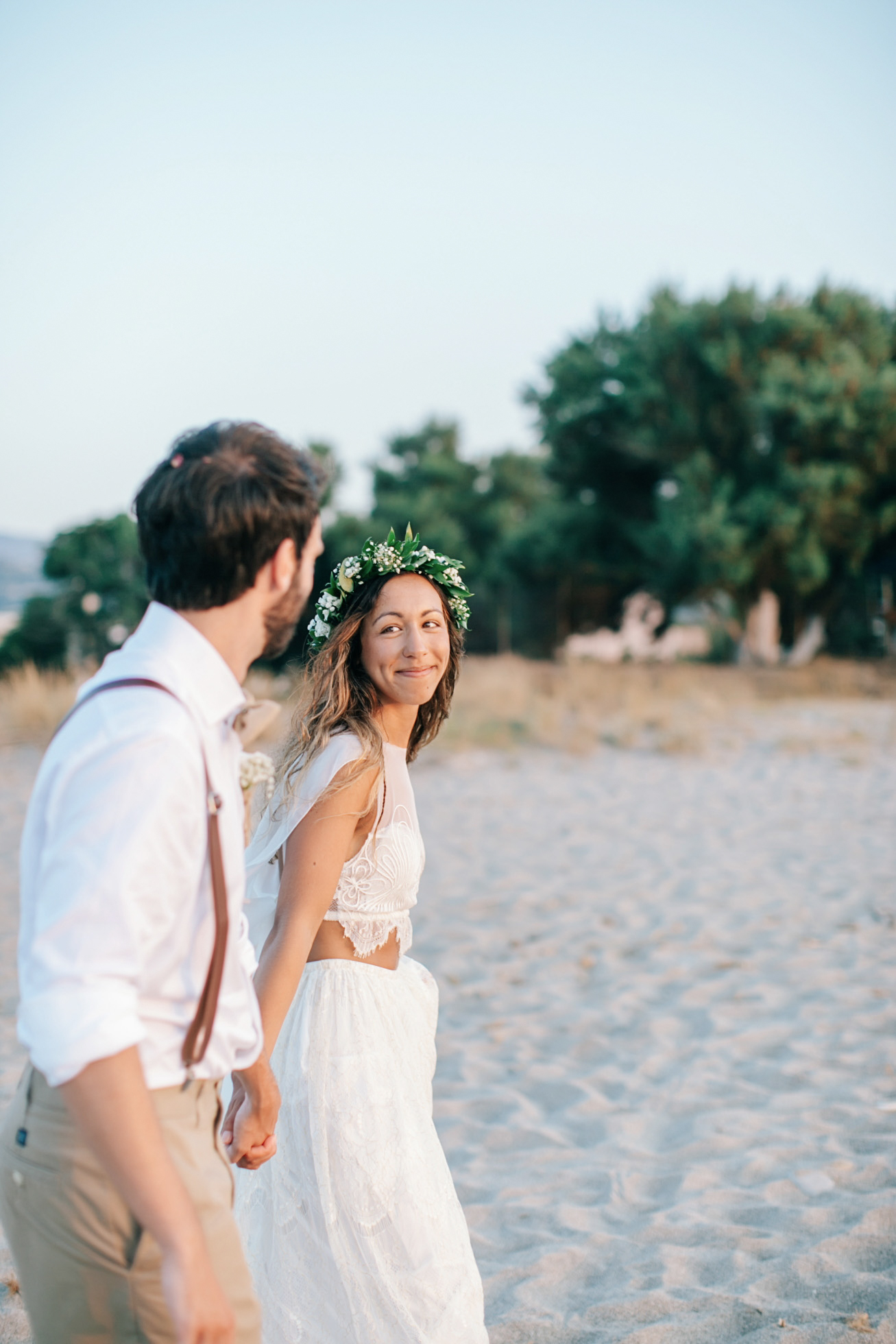 Professional image of bride and groom walking along a sandy beach in Crete after their beach wedding ceremony.