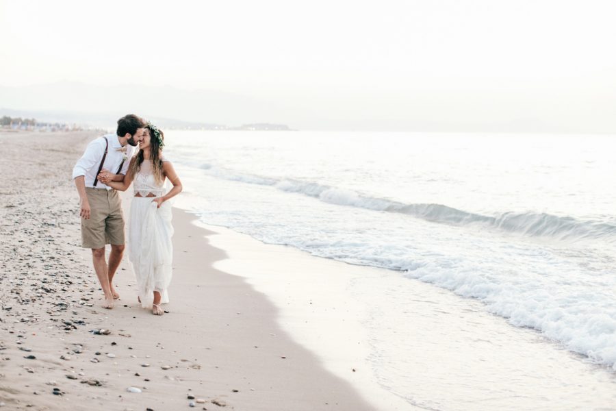 Professional image of bride and groom walking along the seashore on a sandy beach in Crete after their beach wedding ceremony.