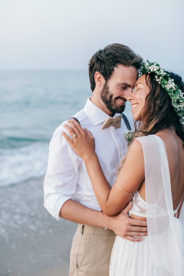 Professional image of bride and groom standing on the sea shore on a sandy beach in Crete after their beach wedding ceremony.