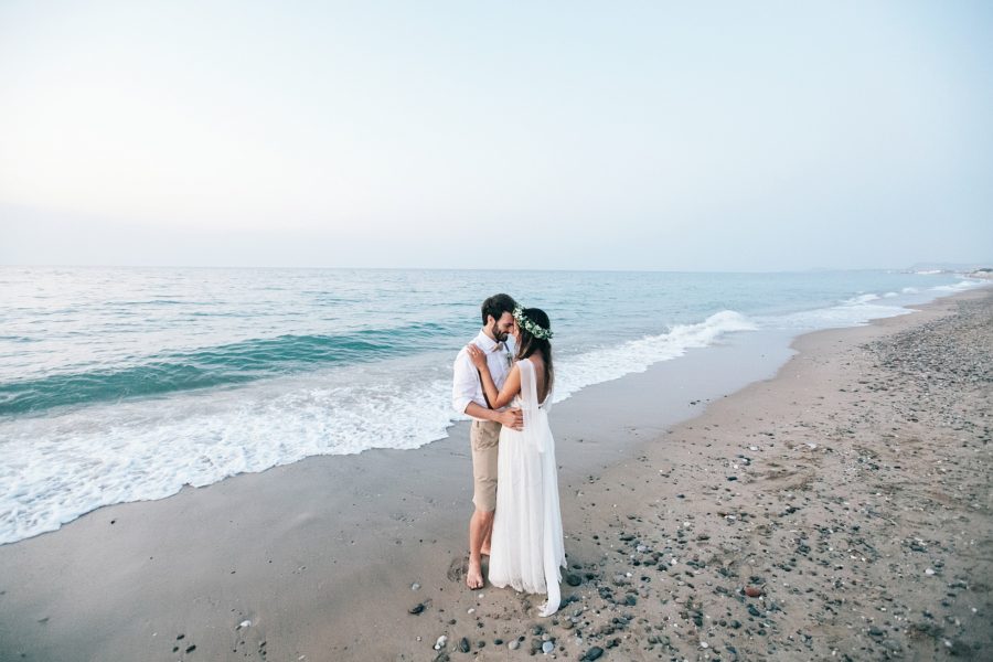 Professional image of bride and groom standing on the sea shore on a sandy beach in Crete after their beach wedding ceremony.