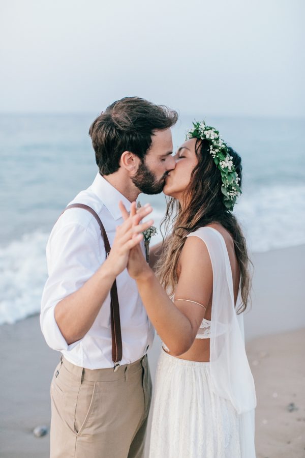 Professional image of bride and groom kissing gently on the sea shore on a sandy beach in Crete after their beach wedding ceremony.