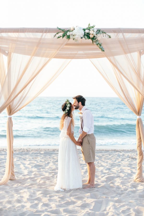 Newlyweds under boho wedding canopy on the beach in Crete island.