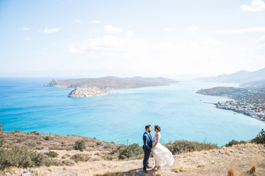 Professional wedding photosession in Elounda Crete, bride and groom walking and posing with Spinalonga island and sea view in the background.