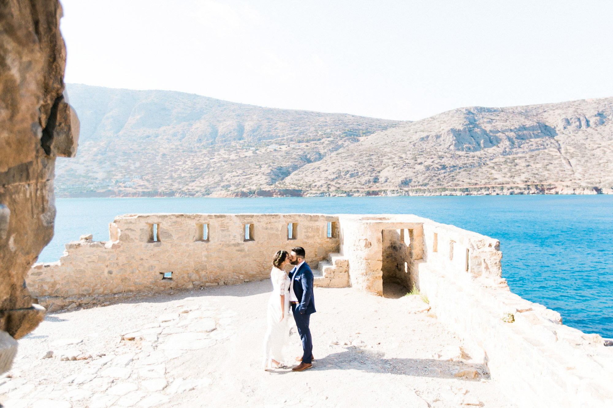 Professional wedding portrait photosession in Crete, bride and groom posing while taking a walk along Spinalonga island, it's historical ruins, church and sites, sea and majestic olive trees in the background.