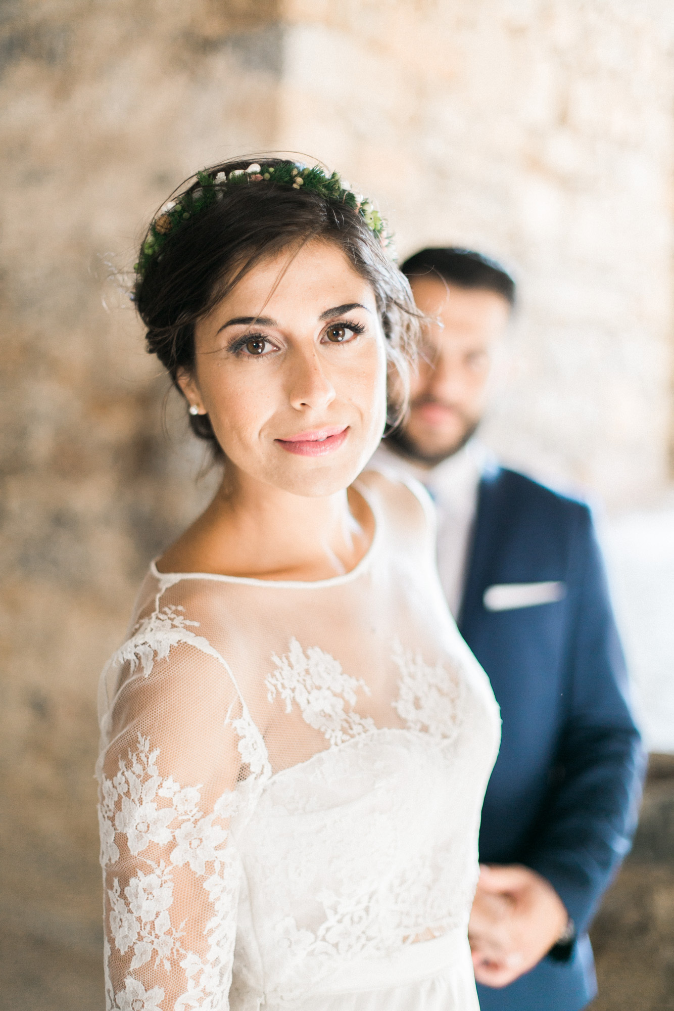 Professional wedding photoshoot in Crete, bride posing with groom with Spinalonga island historical ruins in the background.