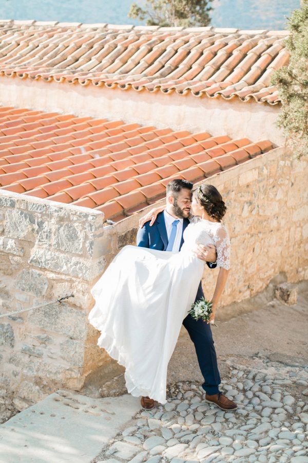 Professional wedding portrait photosession in Crete, bride and groom posing while taking a walk along Spinalonga island, it's historical ruins, church and sites, sea and majestic olive trees in the background.