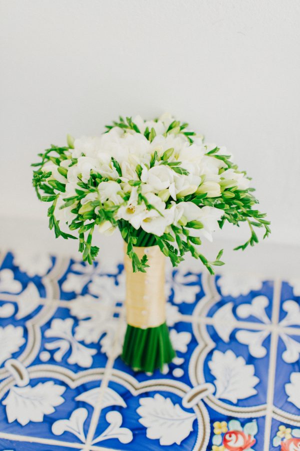 White fresia bridal bouquet styled by wedding photographer on blue mosaic floors in Caramel luxury hotel in Crete.