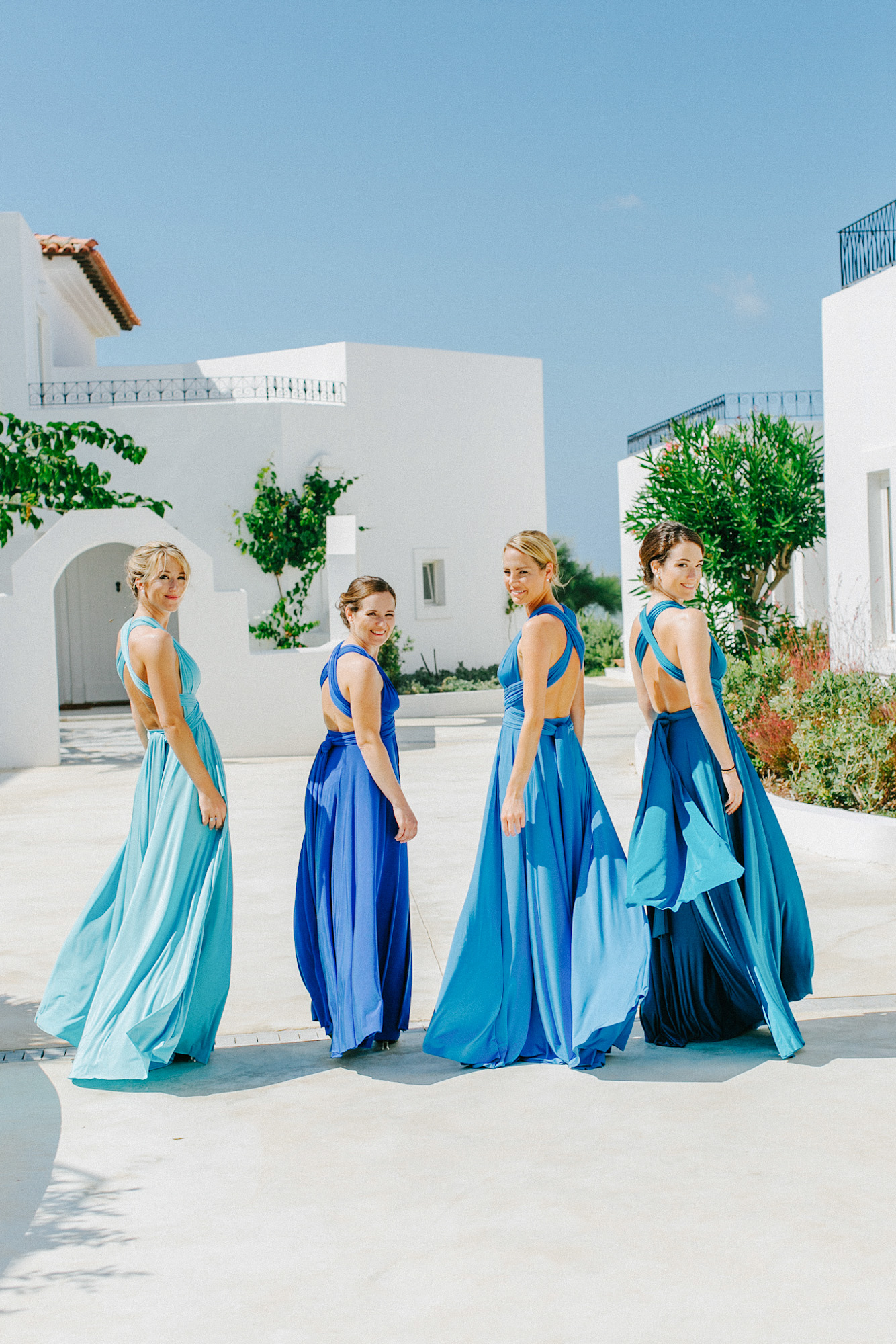 Professional portrait of four bridesmaids walking along Caramel hotel wearing mismatched dresses and looking at the wedding photographer smiling.
