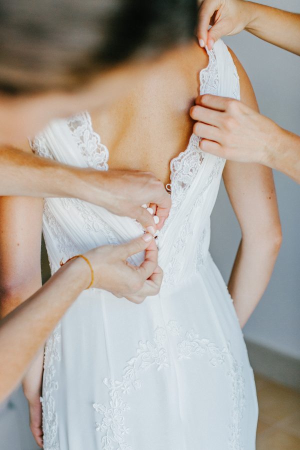 Bridesmaids dressing the bride on her wedding day, a close-up image of their hands fastening the bridal dress.