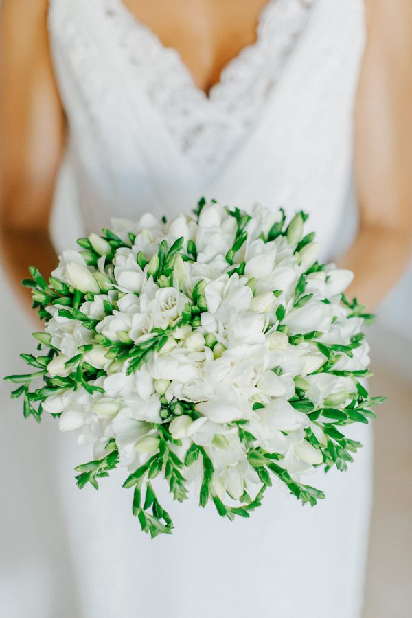 Professional image of a bridal bouquet being held by the bride with the background of white Pronovias dress.