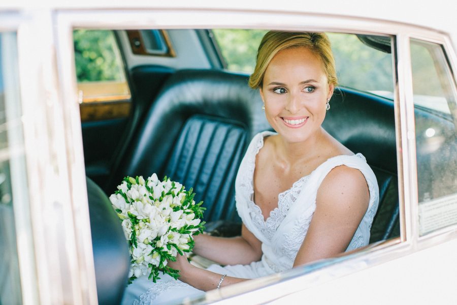 Bride looking out of the window of the luxury bridal car and smiling looking at her groom and guests.
