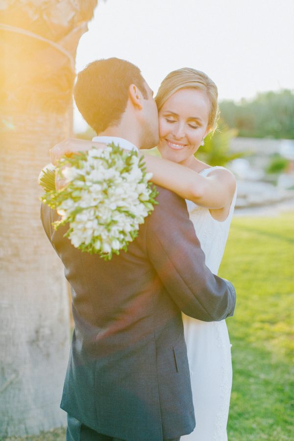 Beautiful sunset portrait of bride and groom posing together for their wedding photographer captured after the wedding ceremony in palm tree wedding estate in Rethymno Crete.