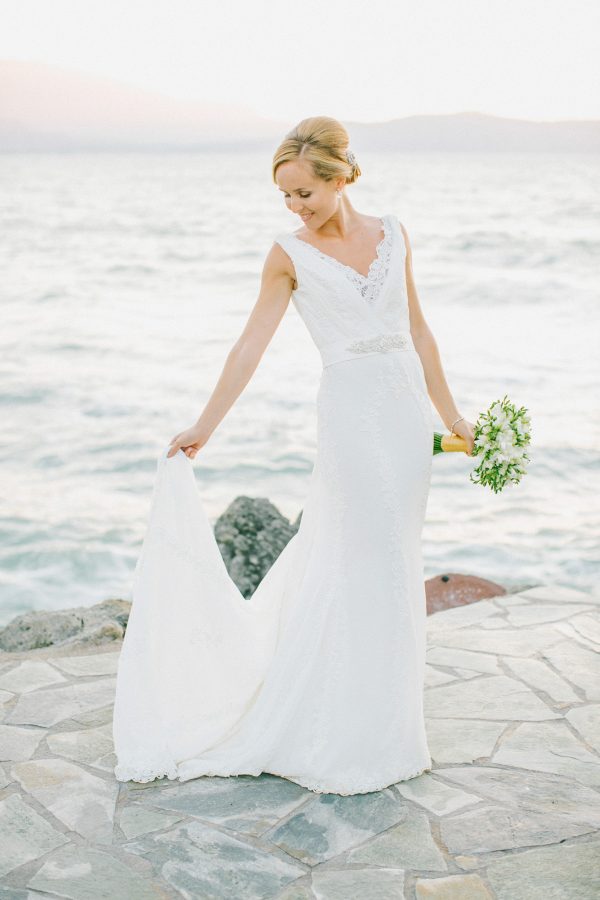 Professional portrait of bride posing for her wedding photographer wearing Pronovias bridal dress and holding flower bouquet captured after the wedding ceremony in palm tree wedding estate in Rethymno Crete with a sunset sea view background.