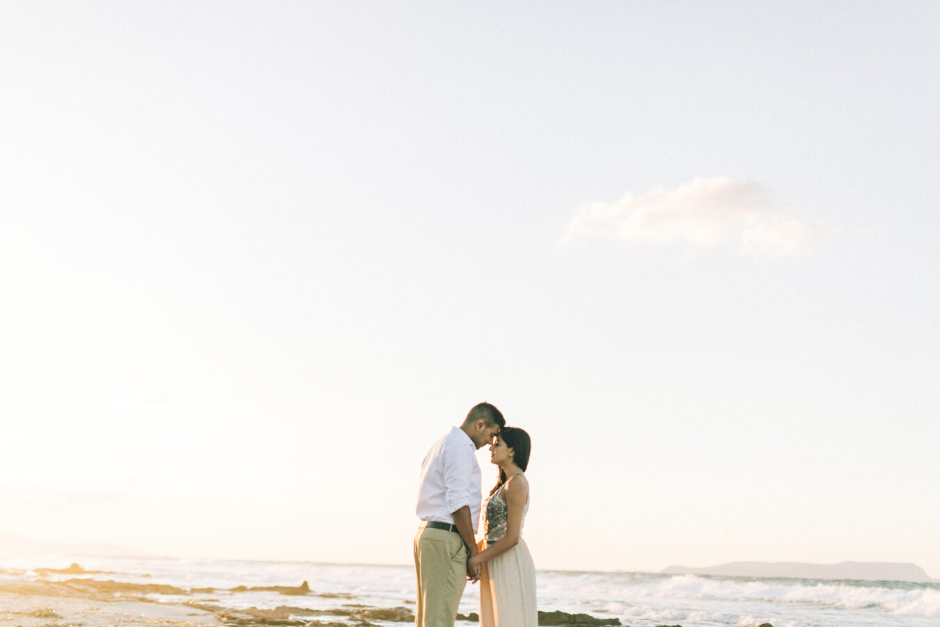 Landscape portrait of young couple holding hands when posing on the beach in Crete during their pre wedding engagement photosession at sunset.