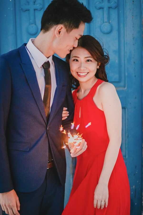 Beautiful Asian couple from Hong Kong is posing for the wedding photographer for their sunset engagement portraits in Imerovigli village Santorini. They're smiling and having good time, wearing formal designer outfits.