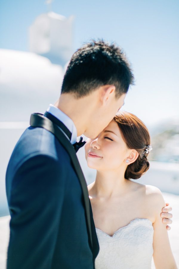 Professional Santorini wedding day photoshoot, groom and bride are posing with the picturesque background of Oia, seaview and clear blue skies.