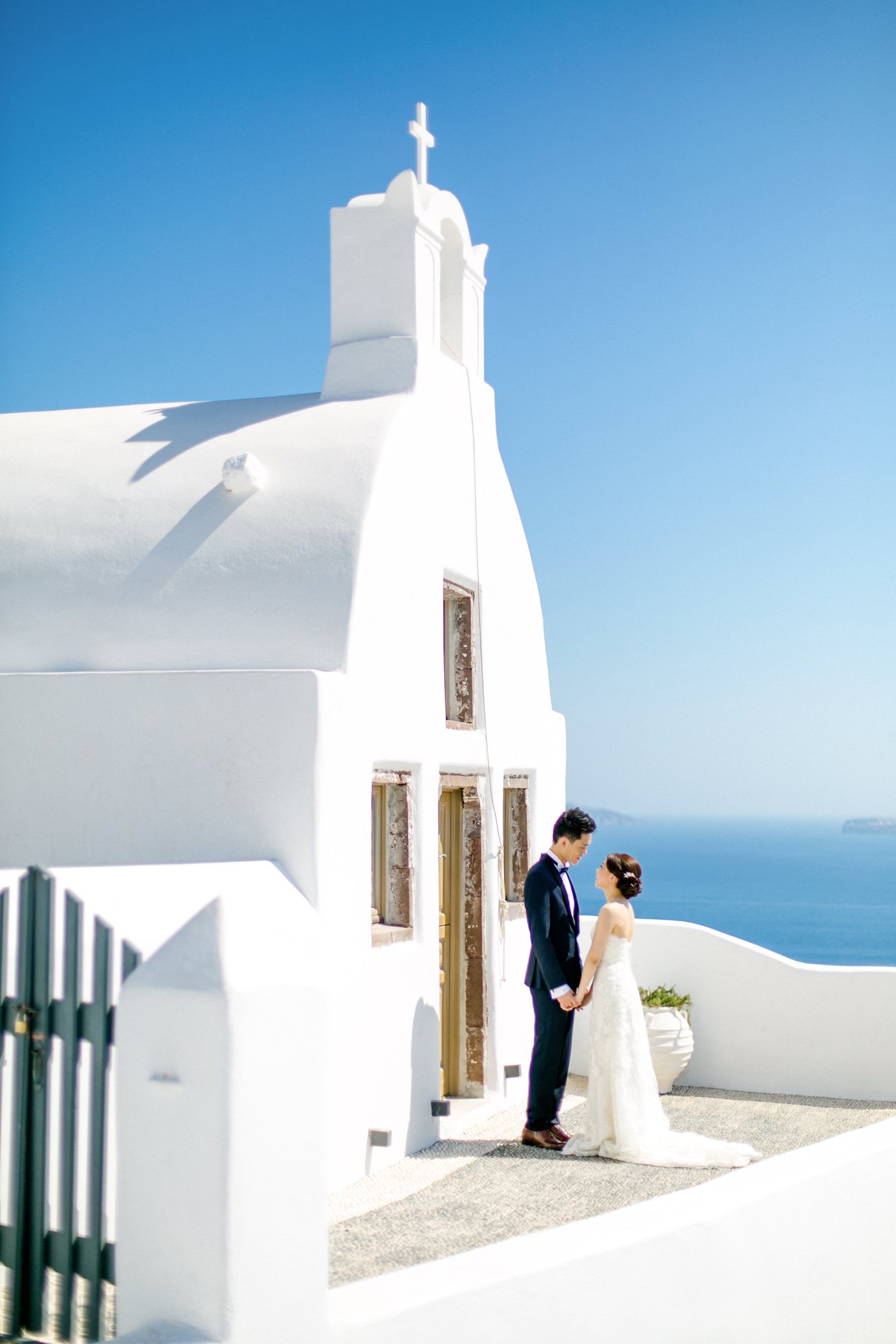 Professional Santorini wedding day photoshoot, groom and bride are posing with the picturesque background of Oia, seaview and clear blue skies.