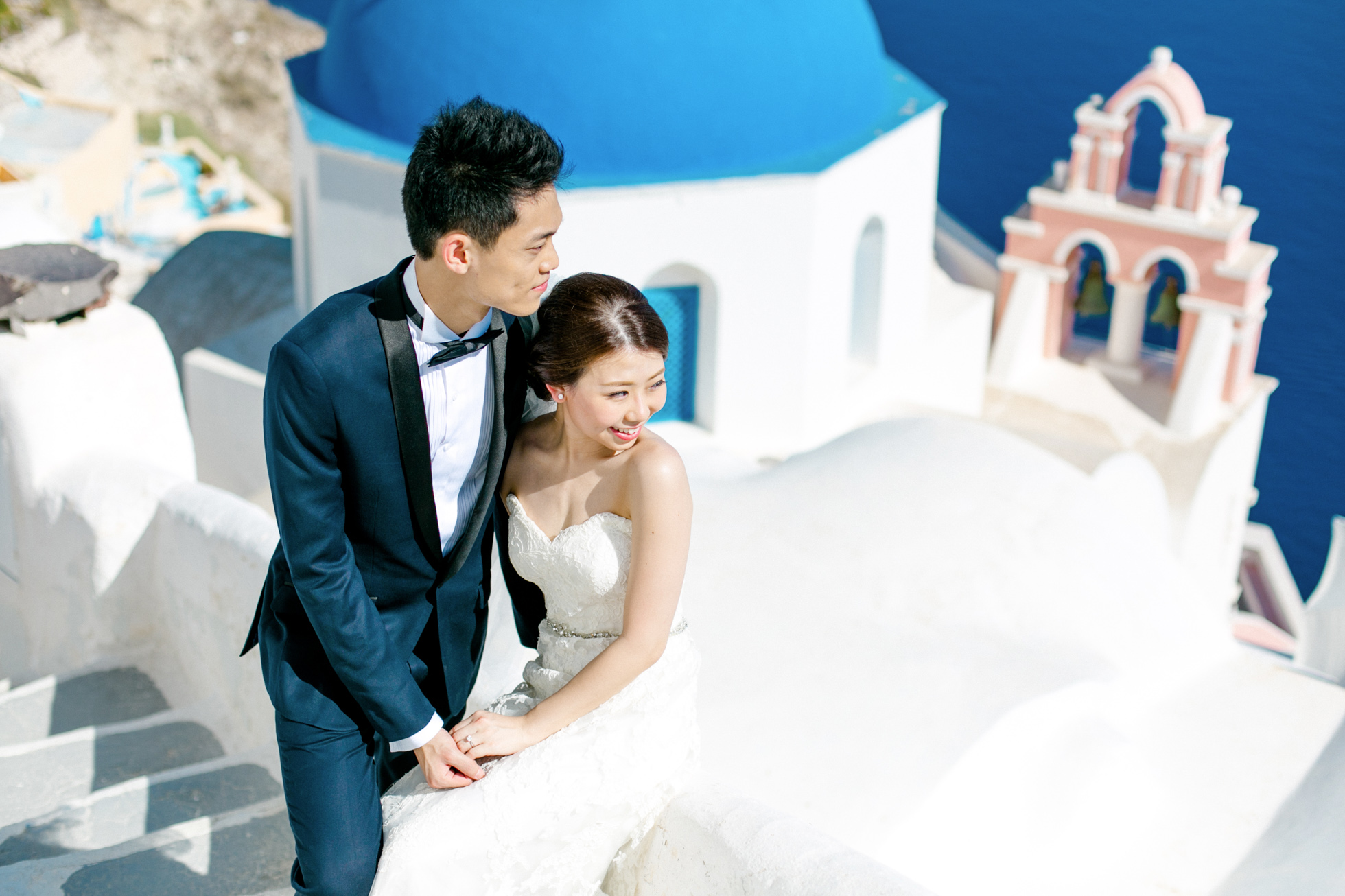 Professional Santorini wedding day photoshoot, groom and bride are posing with the picturesque background of Oia, seaview and clear blue skies.