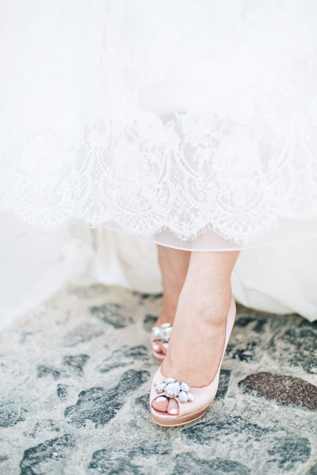 Professional Santorini wedding day photoshoot, close up photograph of bride's wedding dress and shoes while she's walking the pebbled streets of Oia. Light pink bridal shoes made by MiuMiu shoe brand.