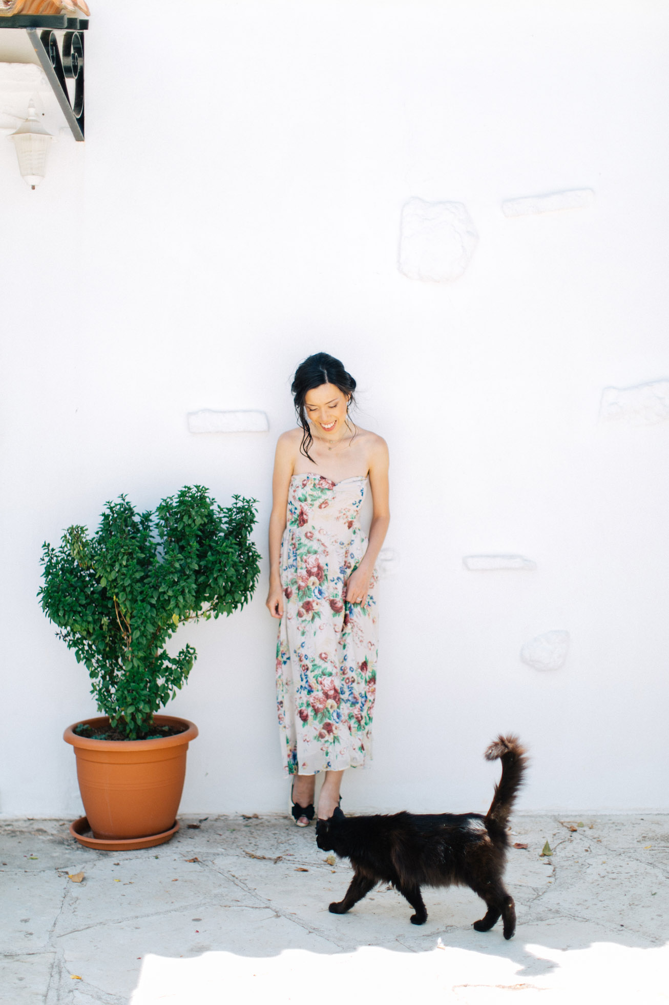 Young elegant woman wearing summer dress and elegant makeup is posing for her elopemement portraits for professional photographer team in Crete island, Greece. Colorful garden and park backdrop adds to the happy and vibrant feel of this session.