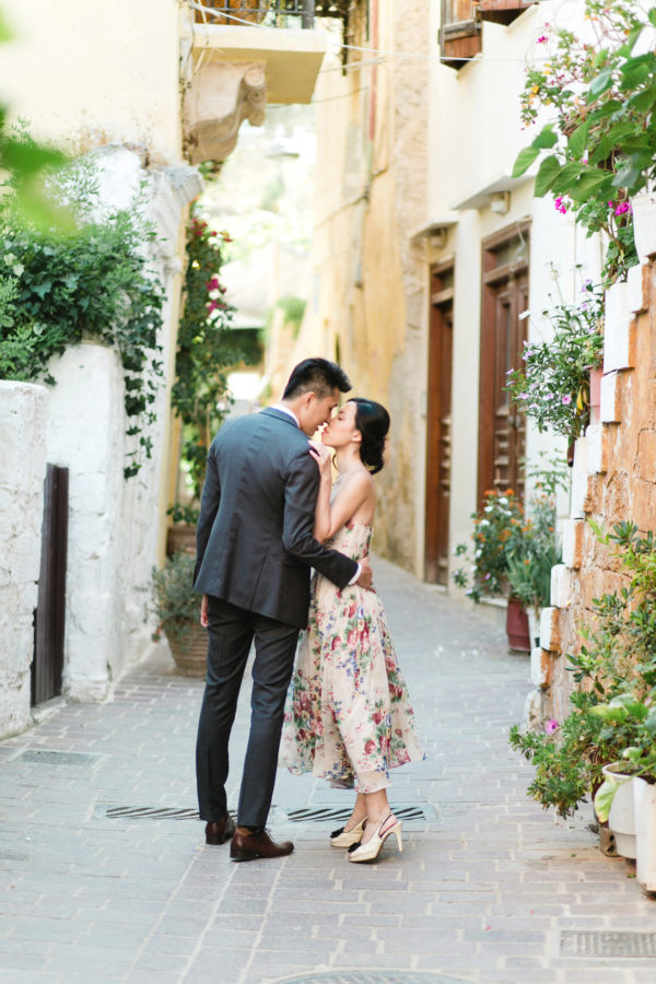 Young Asian couple in love during their engagement portrait session in old town of Chania, Crete. They're hugging and posing for photos with the backdrop of Greek architecture.
