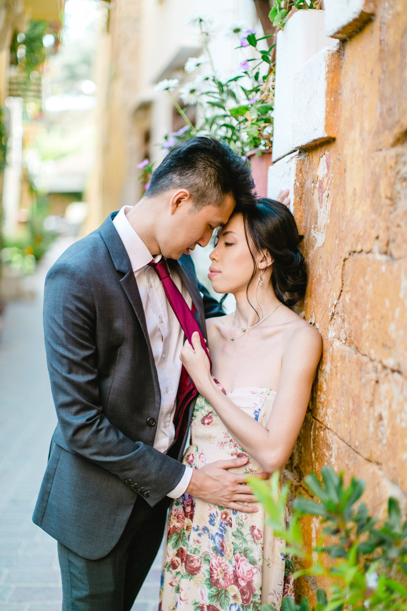 Young Asian couple in love during their engagement portrait session in old town of Chania, Crete. They're hugging and posing for photos with the backdrop of Greek architecture.