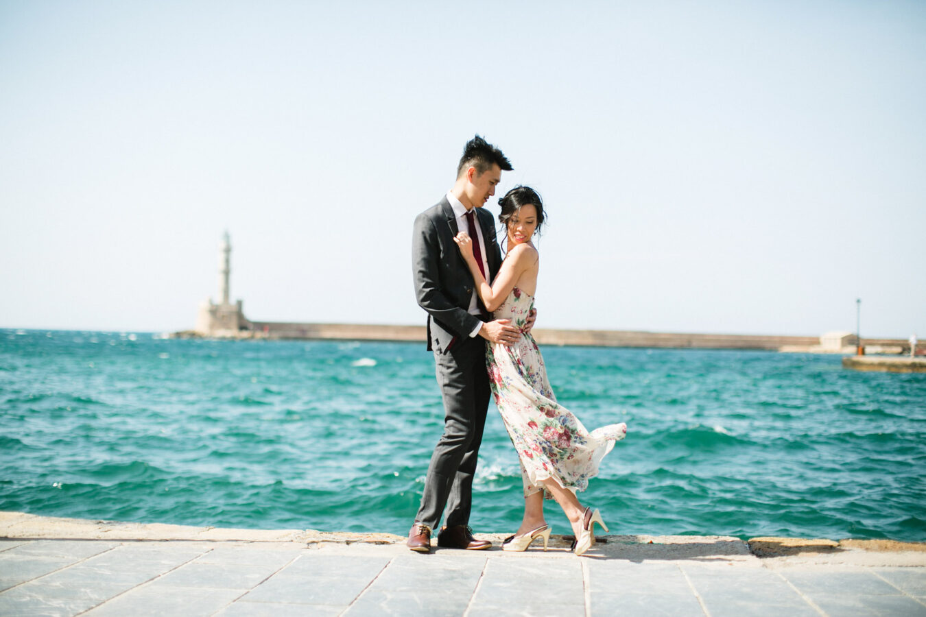 Young Asian couple in love during their engagement portrait session in the harbour and port of Chania, Crete. They're having fun and posing for photos with the backdrop of sea.