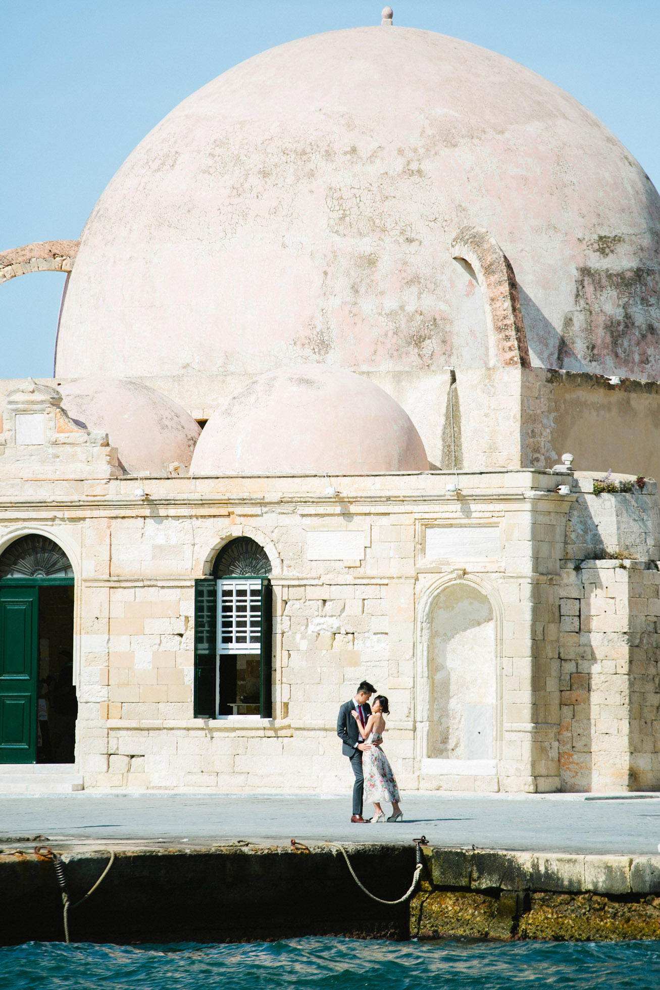 Young Asian couple in love during their engagement portrait session in the harbour and port of Chania, Crete. They're having fun and posing for photos with the backdrop of sea.