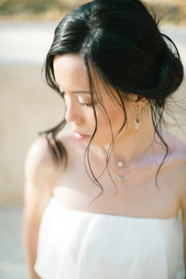 Elegant Asian bride wearing white understated and posh bridal dress posing for professional photographer for her wedding portraits in Fortezza of Rethymno town, Crete.