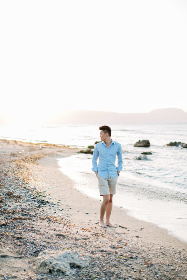 Young good looking man wearing summer clothing is posing for professional photographer team during his beach destination photoshoot on the secluded shores of Rethymno town, Crete, Greece.