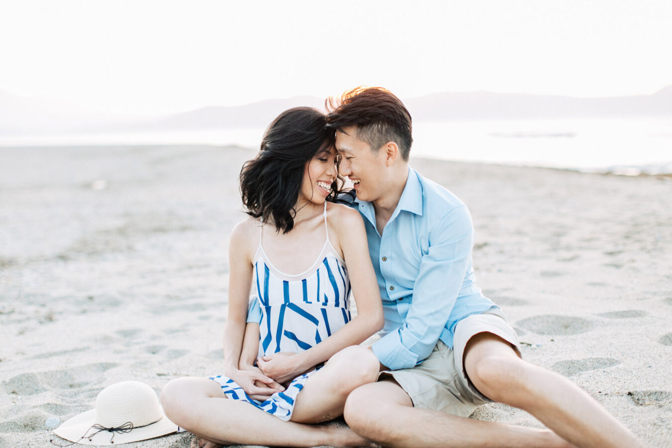 Happy international couple wearing summer clothing is posing for professional photographer team during their beach wedding photoshoot on the secluded shores of Rethymno town, Crete, Greece.