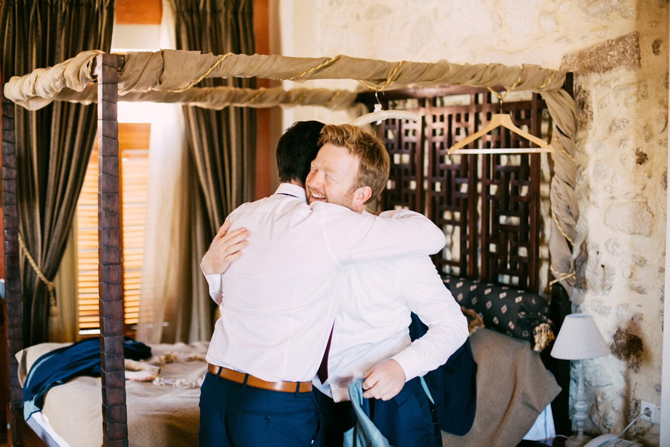 Groom's preparations portraits photographed in Avli hotel Rethymno during destination wedding in Crete. Groom and best man smiling and enjoying their time together during the wedding preparations stage in groom's hotel suite.