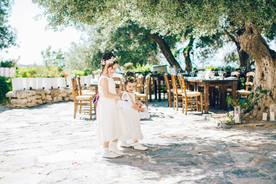 Candid image of two cute flower girls walking down the aisle into the wedding ceremony on a destination wedding day in Agreco Farm in Crete.