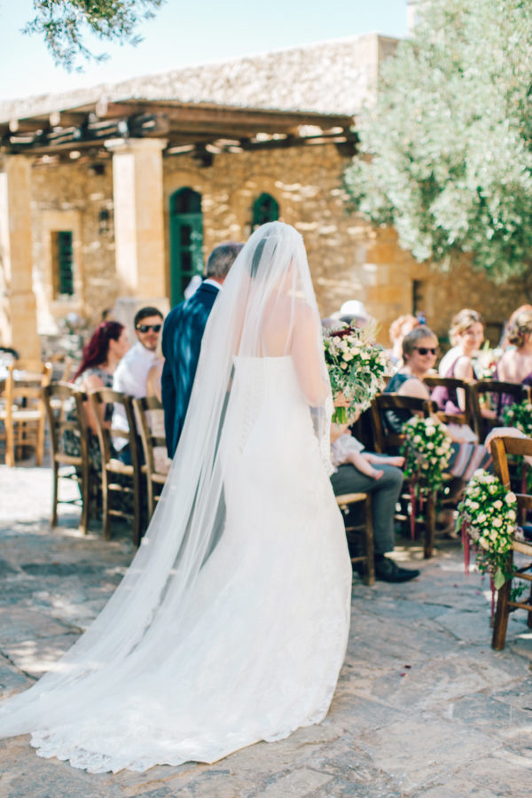Candid image of elegant bride walking down the aisle into the wedding ceremony on a destination wedding day in Agreco Farm in Crete.