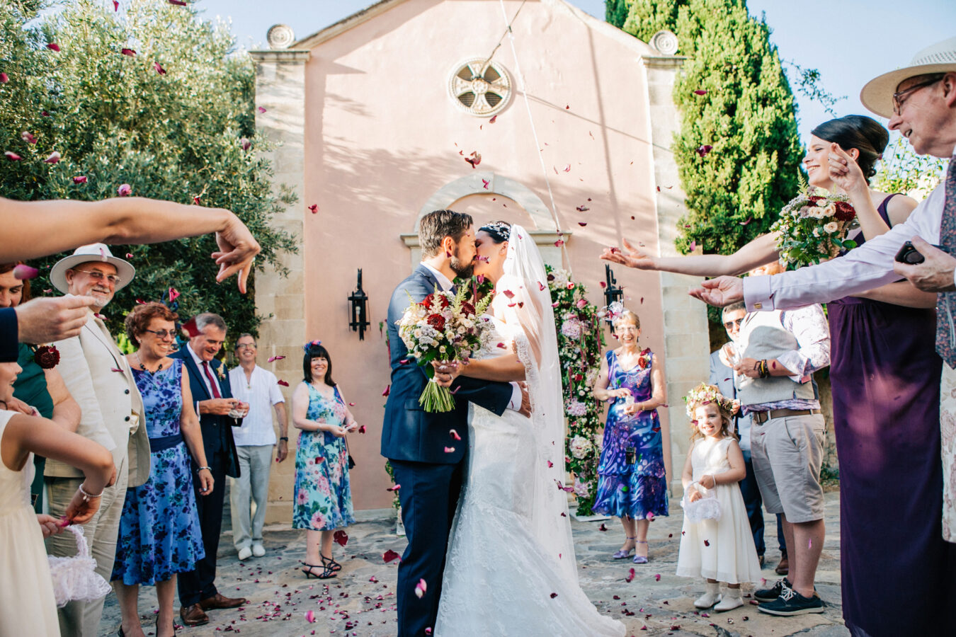Candid image of bride and groom after their wedding ceremony at Agreco Farm in Crete, Greece. Guests are having fun and throwing rose petals for the newlyweds.