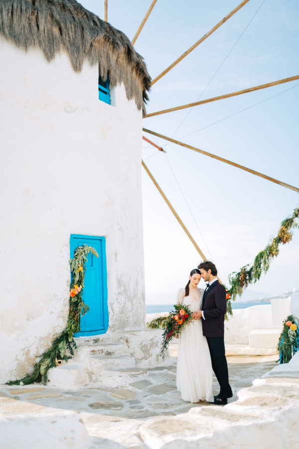 Stylish bride and groom on their destination wedding in Mykonos, posing under the windmills.