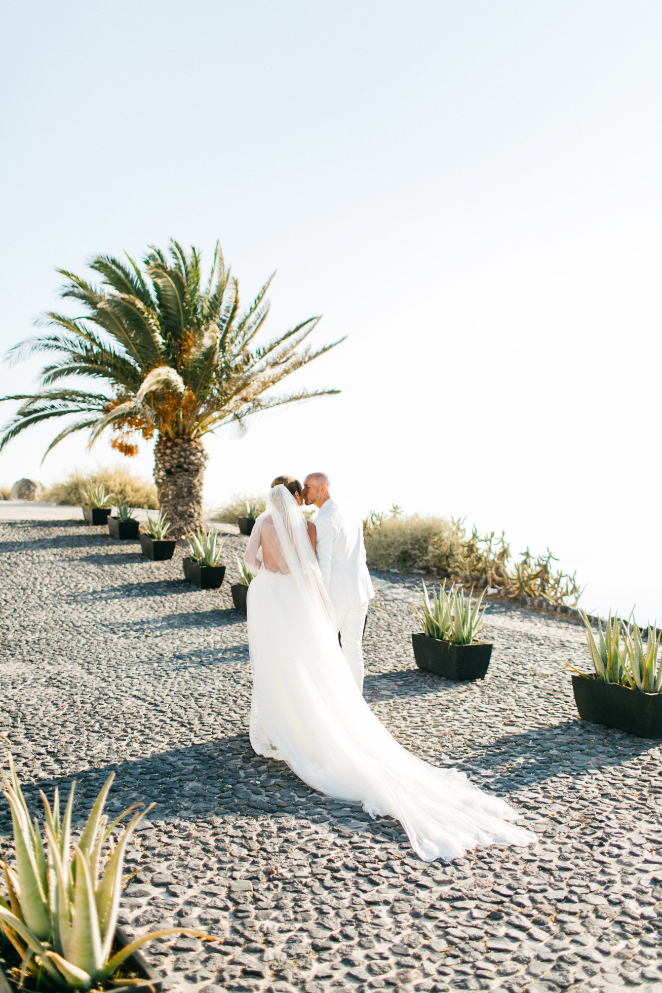 Bride and groom posing for their wedding day portraits on a cliffside near Le Ciel wedding estate in Santorini island, Greece.