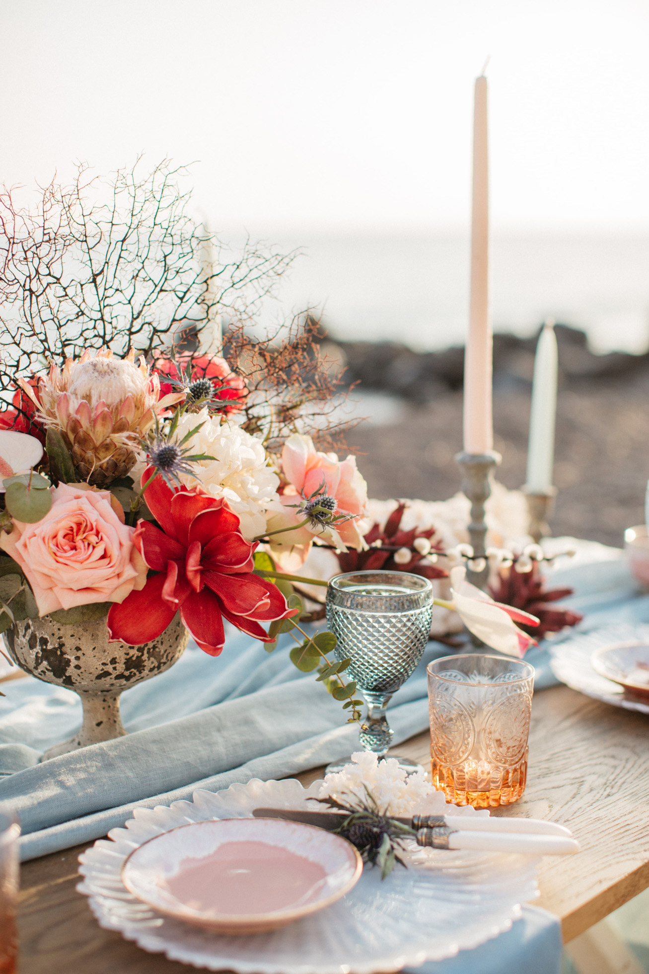 Vibrant wedding dinner and reception beach table setup in Santorini accented with coral and exotic florals.