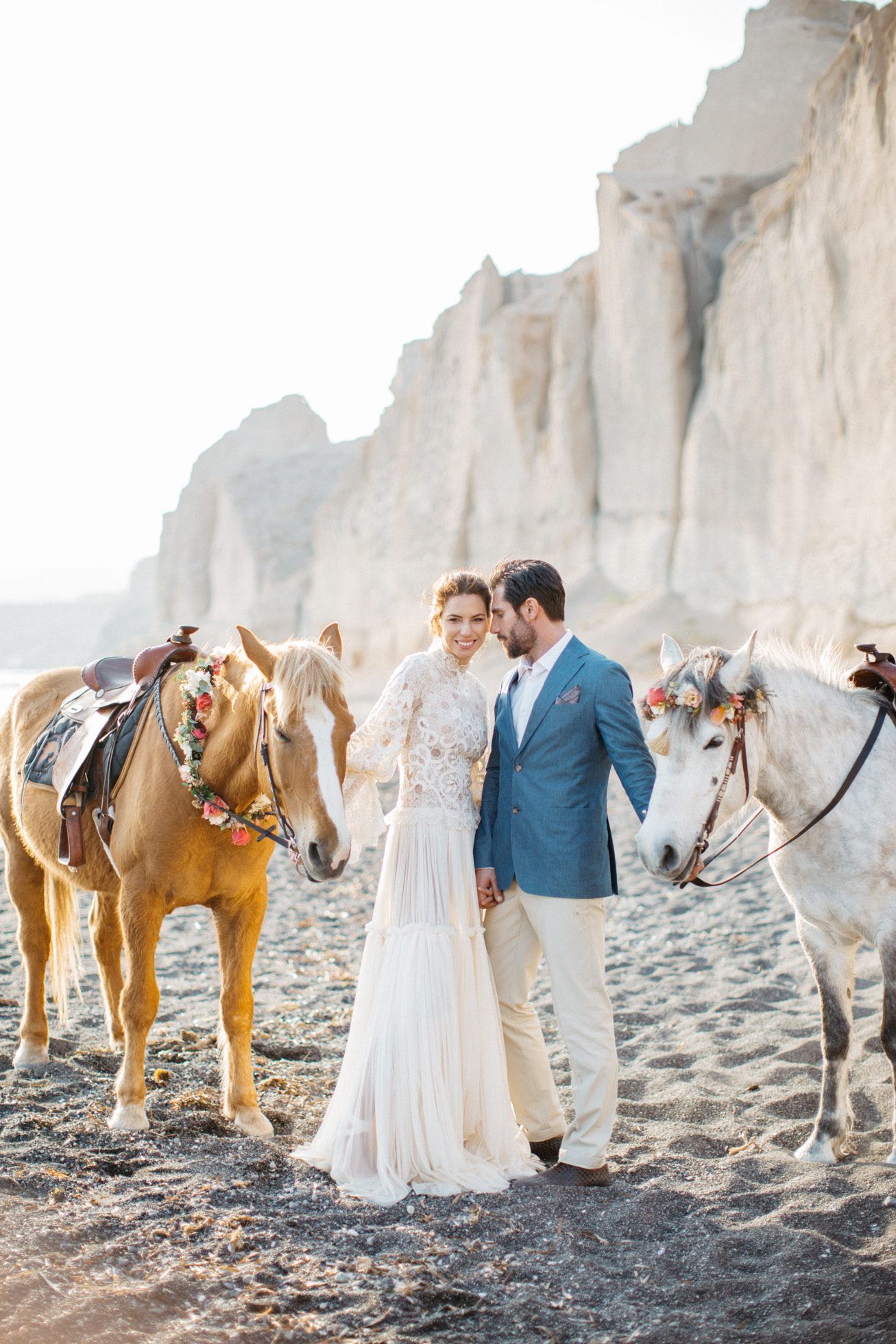 Beautiful romantic bride and groom with horses at a volcanic beach wedding inspiration session in Santorini Greece.
