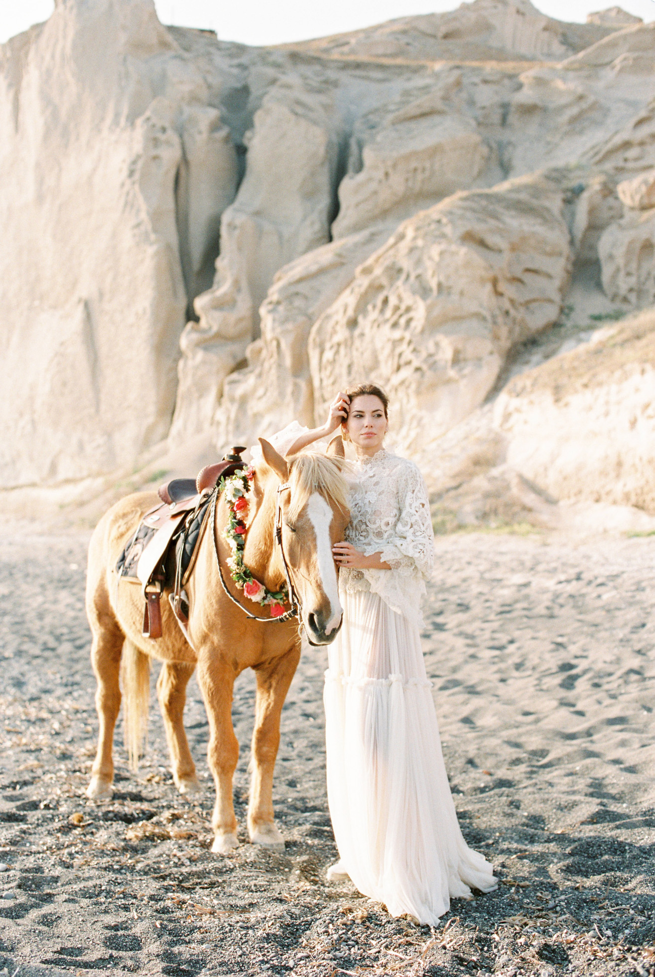 Beautiful bride wearing designer wedding dress holding a horse at a volcanic beach wedding inspiration session in Santorini Greece.