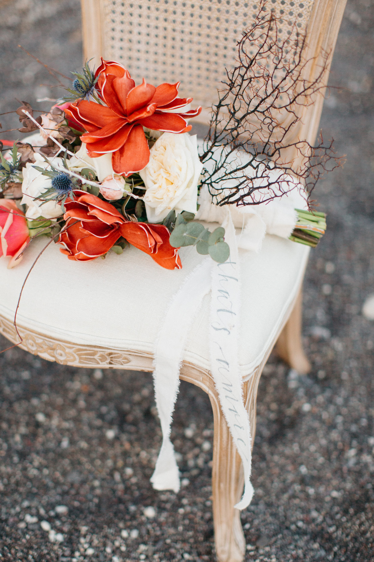 Unique floral wedding bouquet and furniture on the black sand volcanic beach in Santorini Greece.
